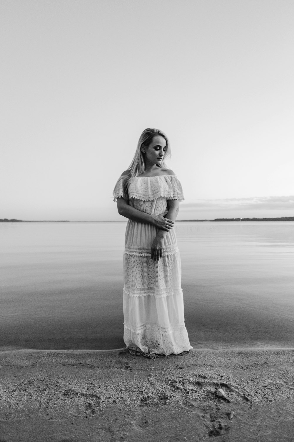 grayscale photo of woman in dress standing on beach