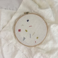 Close-up of a whimsical needlepoint hoop featuring playful animal designs in pastel colors.