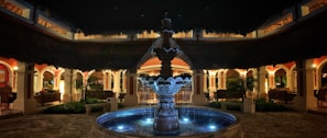 Serene outdoor courtyard with a fountain, surrounded by desert plants under soft twilight.