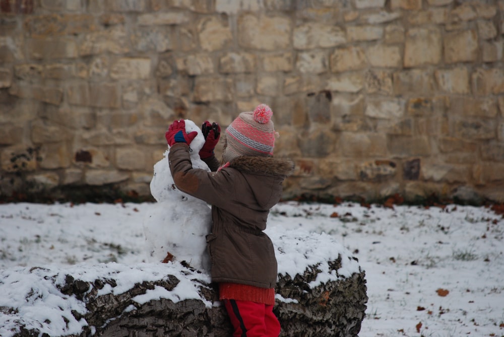 child in brown jacket and red pants holding red snow shovel