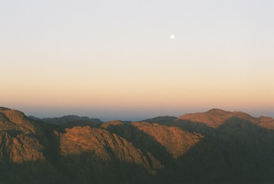 Moonlight casting a soft glow over a quiet river surrounded by forested mountains.