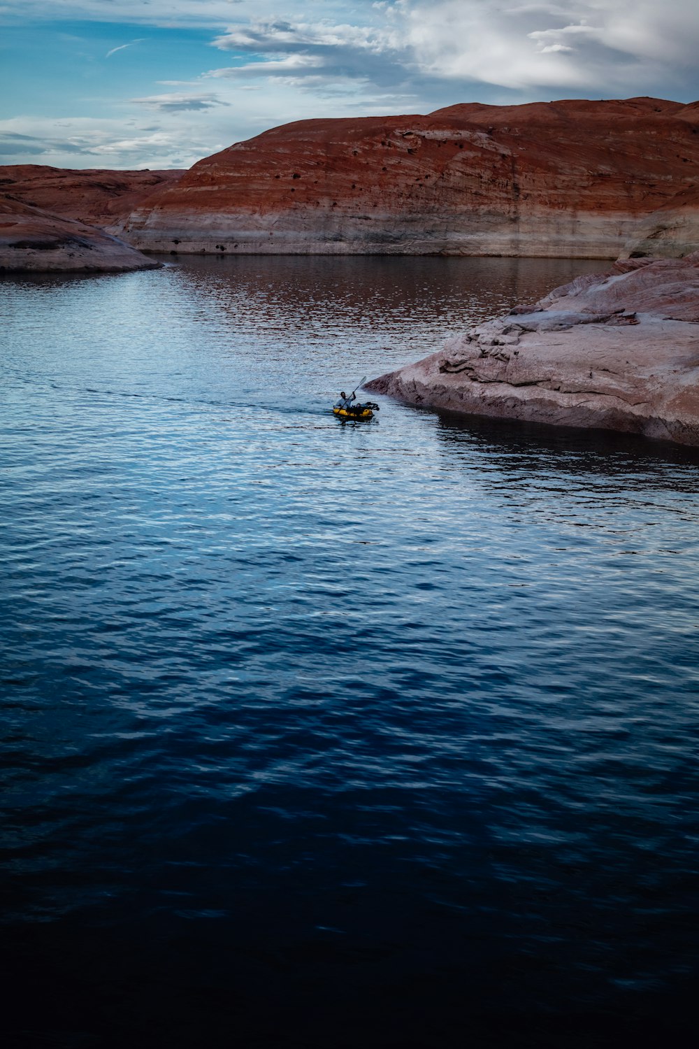 person in blue shirt sitting on rock near body of water during daytime