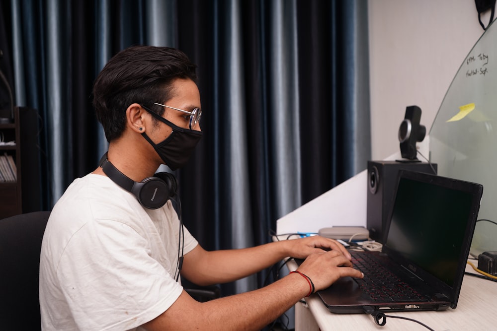 uomo in maglietta girocollo bianca usando il computer portatile nero