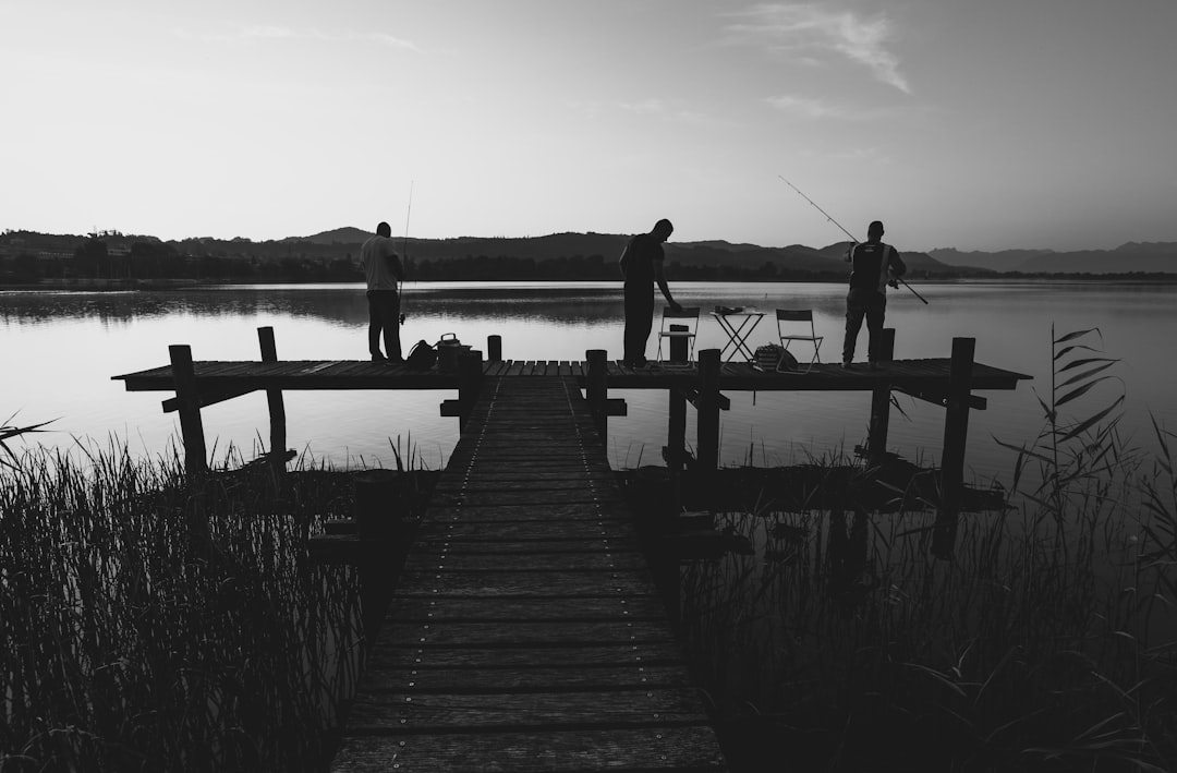 grayscale photo of 2 men standing on wooden dock