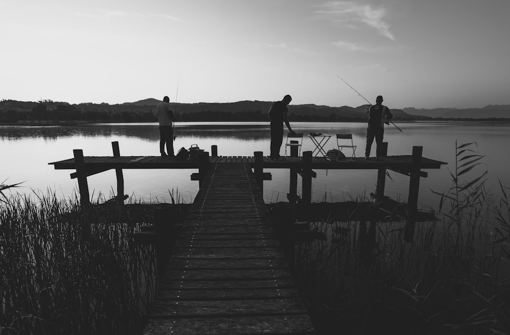 grayscale photo of 2 men standing on wooden dock