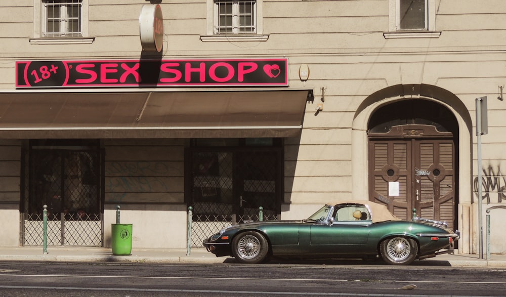 a green car parked in front of a sex shop