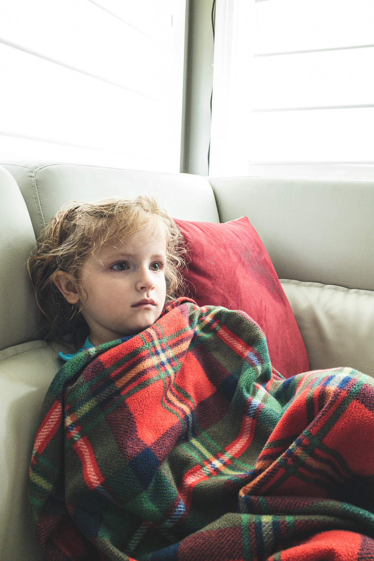Young child wrapped in a plaid blanket resting on a couch, a low-energy sick-day activity