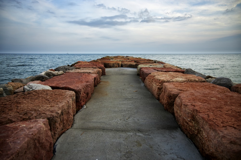 brown concrete pathway on sea shore under cloudy sky during daytime