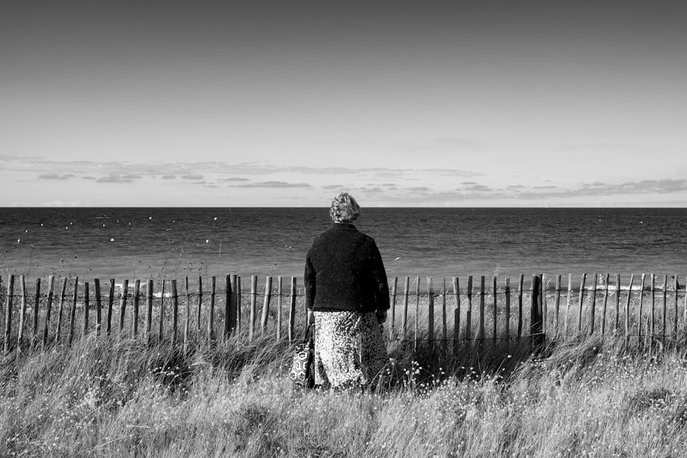 昼間、水辺の柵の上に立つ黒いジャケットを着た男性