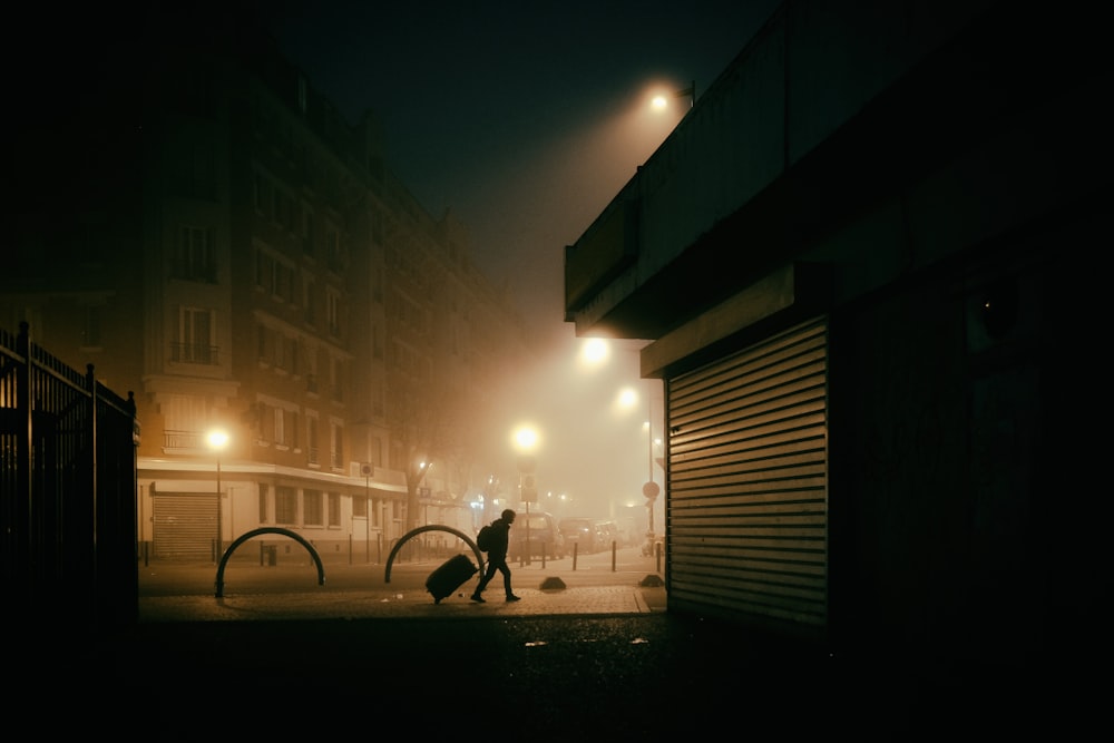 Hombre en chaqueta negra y pantalones caminando en la acera durante la noche
