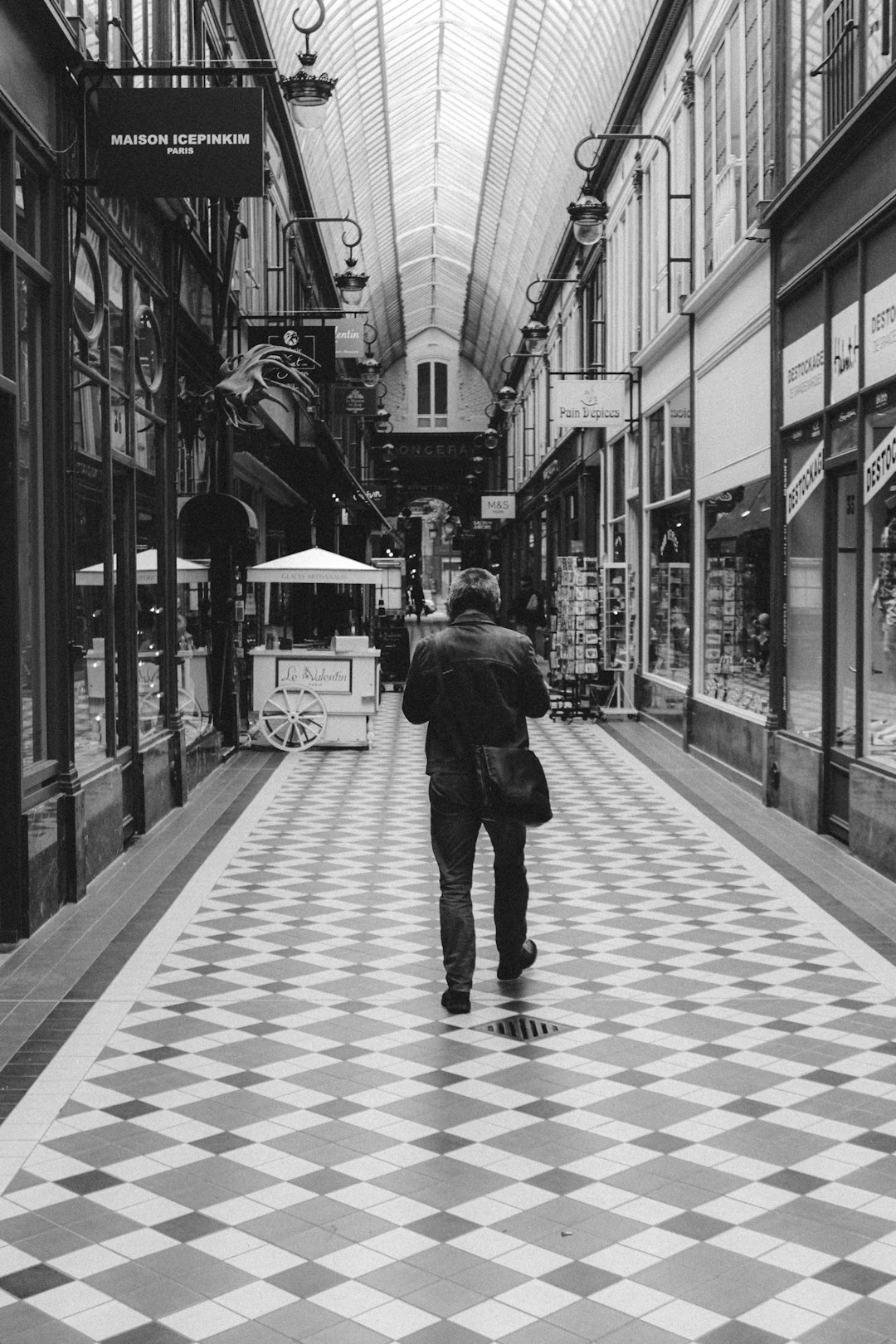 grayscale photo of woman in black jacket and black pants walking on sidewalk