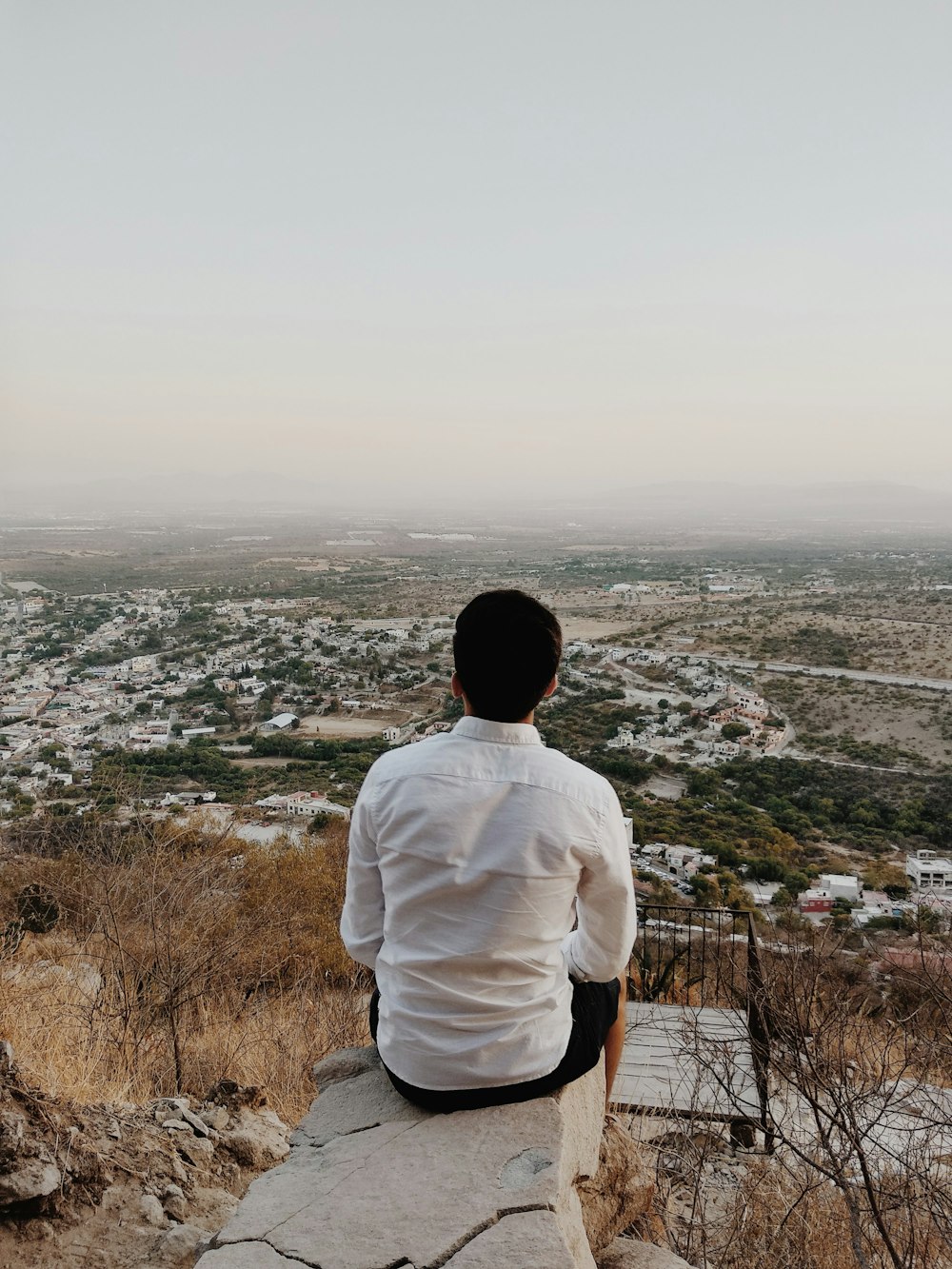 man in white shirt standing on top of the mountain during daytime