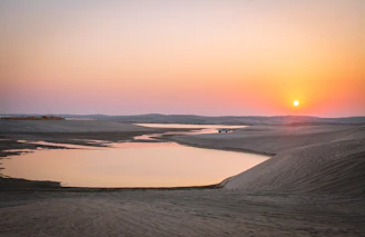 A warm sunset over the Merzouga dunes with a 4x4 vehicle parked nearby.