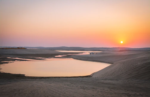 A warm sunset over the Merzouga dunes with a 4x4 vehicle parked nearby.