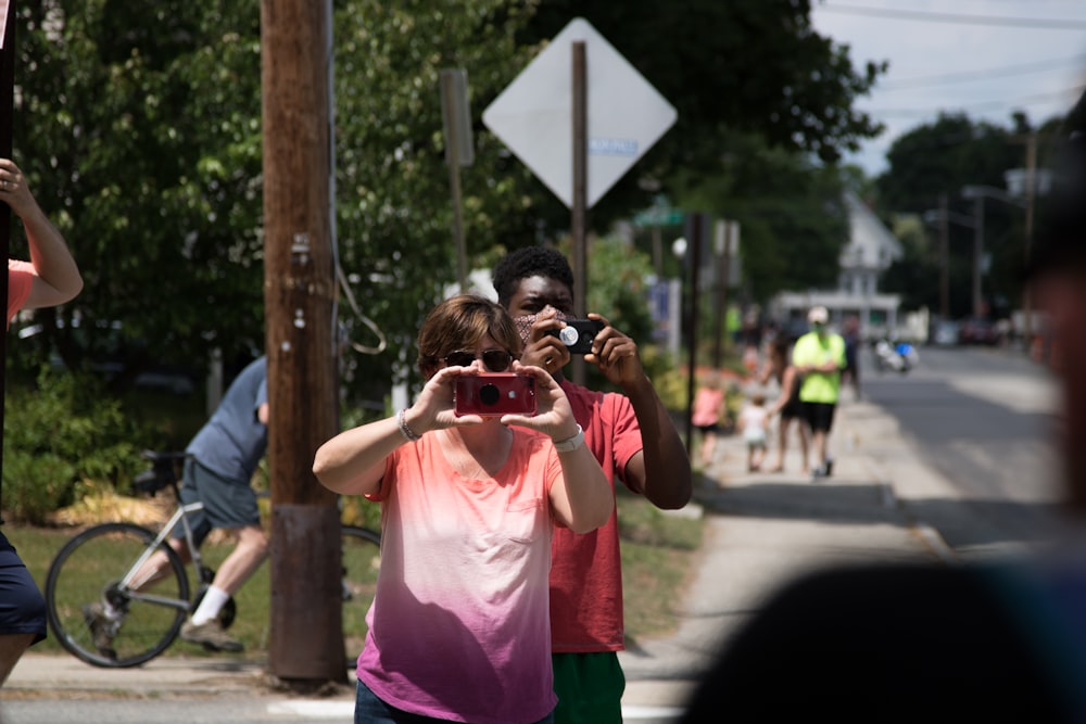 girl in pink shirt holding black camera taking photo of gray road during daytime