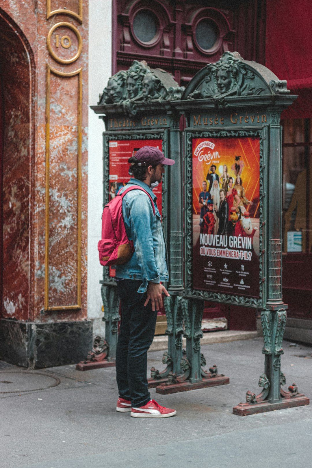 man in red shirt and blue denim jeans standing in front of black wooden door