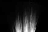 Fiber optic strands illuminated from below, creating a soft, bright glow against a dark background. The strands fan out, resembling a spray or fountain.