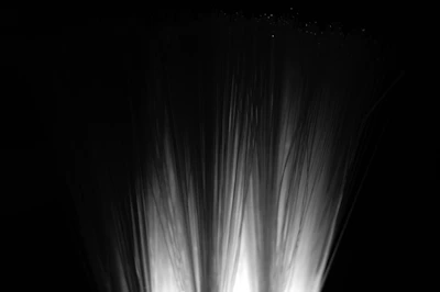 Fiber optic strands illuminated from below, creating a soft, bright glow against a dark background. The strands fan out, resembling a spray or fountain.