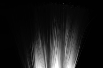 Fiber optic strands illuminated from below, creating a soft, bright glow against a dark background. The strands fan out, resembling a spray or fountain.