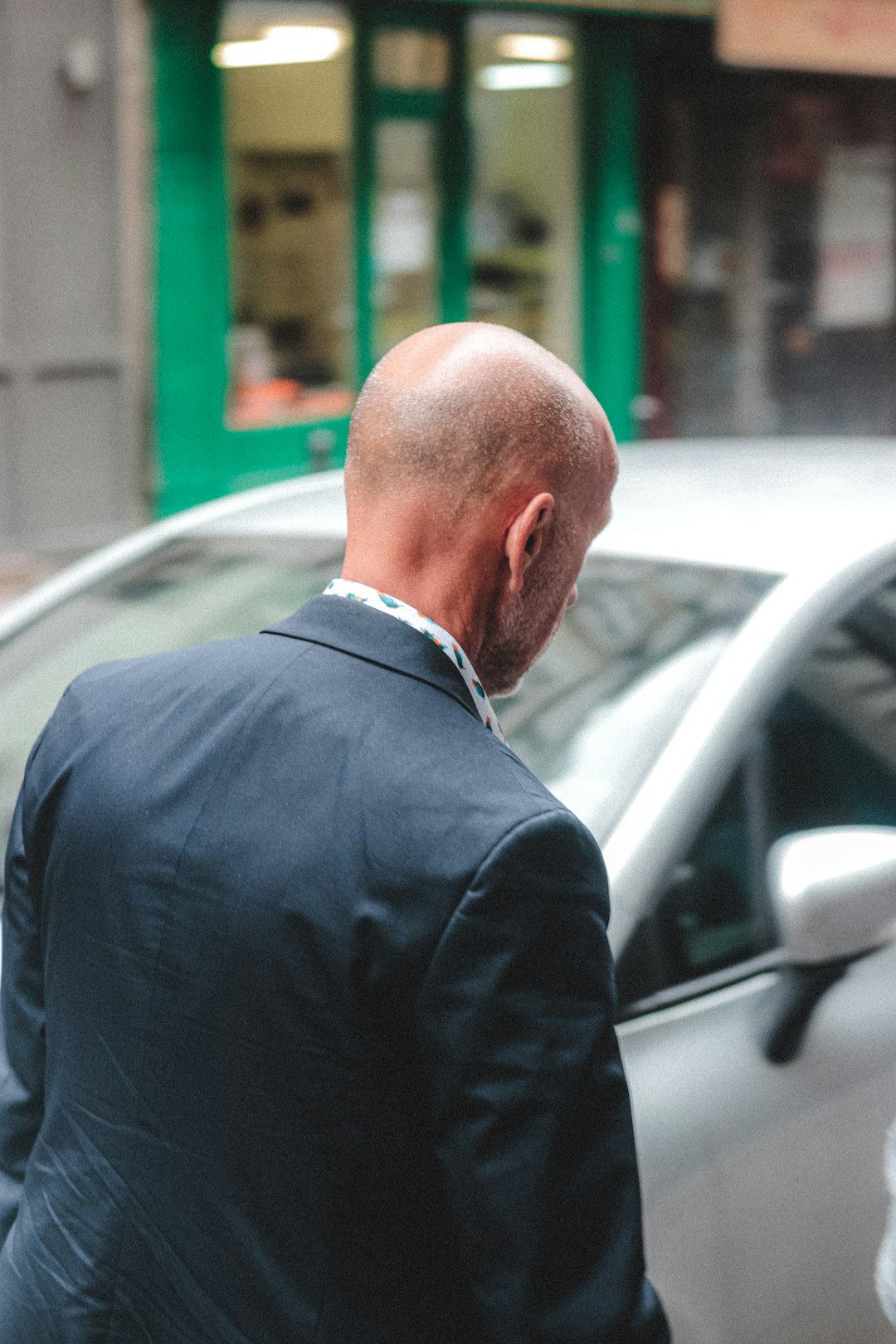 man in black suit jacket standing beside white car during daytime