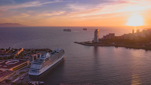Sunset casting golden hues over a modern cruise liner docked at a vibrant port.