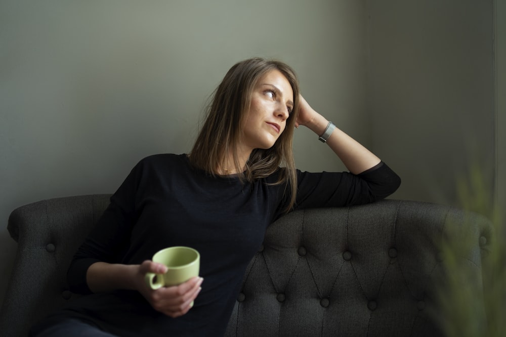 Frau in schwarzem Rundhals-T-Shirt mit grünem Keramikbecher sitzt auf schwarzem Sofa