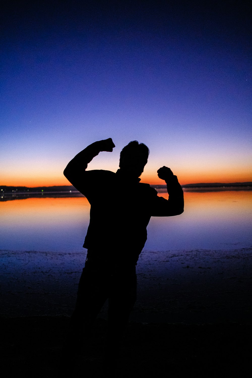 silhouette of man standing near body of water during sunset