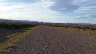 A wide rural gravel road stretching into the distance with rolling fields on either side.