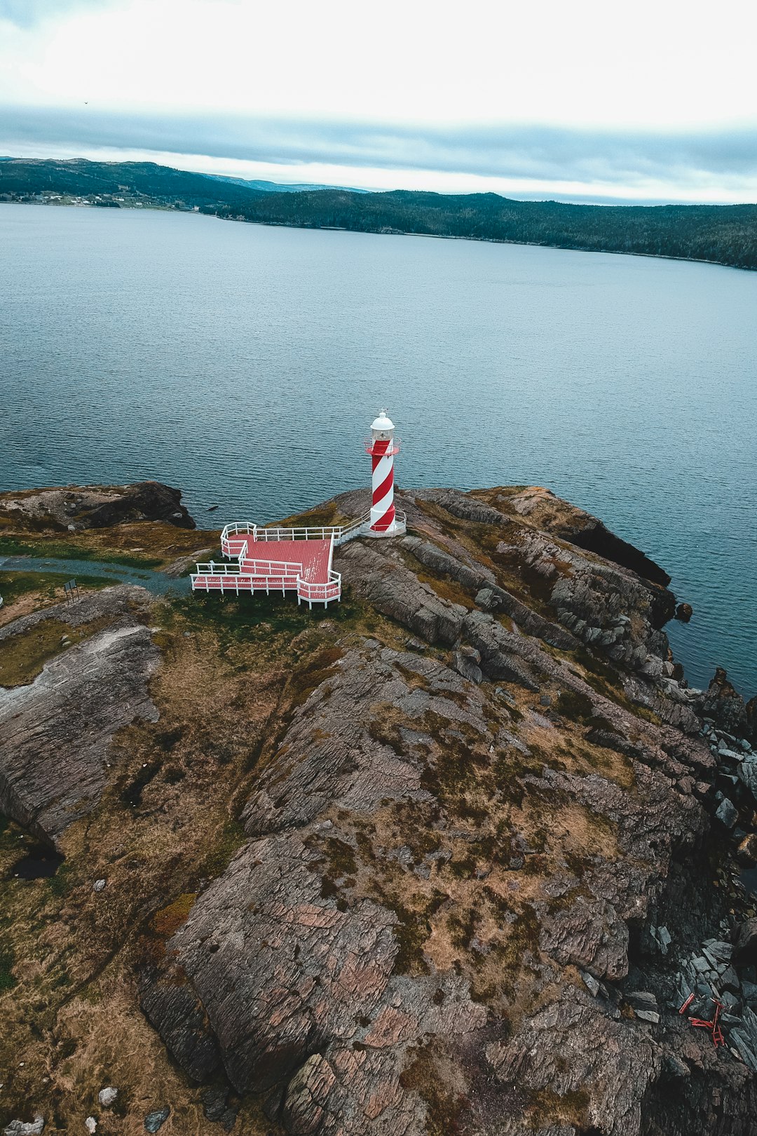 white and red lighthouse on brown rock formation near body of water during daytime