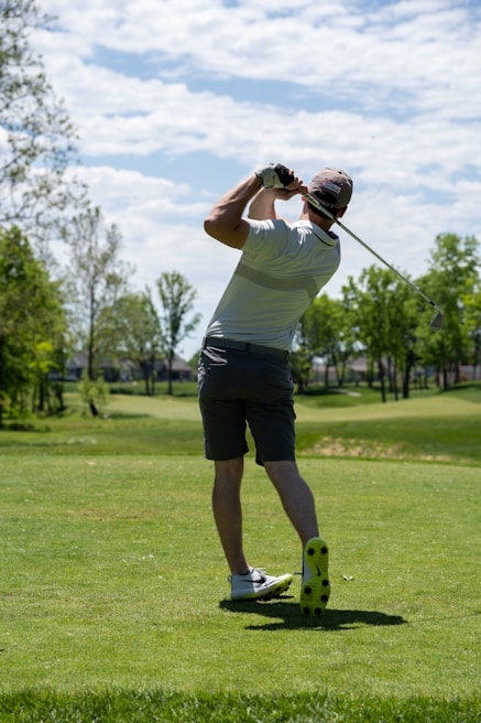 A golfer mid-swing on a sunlit course, dressed sharply in casual golf wear.