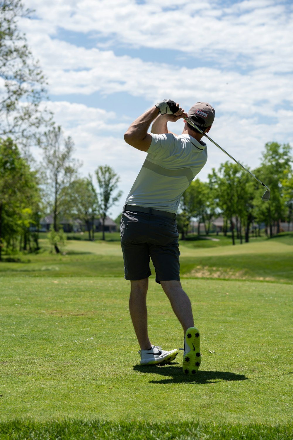 uomo in maglietta bianca e pantaloncini neri che tiene la mazza da golf