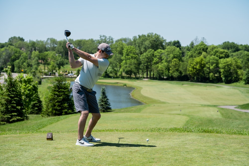 Hombre con camiseta blanca y pantalones cortos negros jugando al golf durante el día