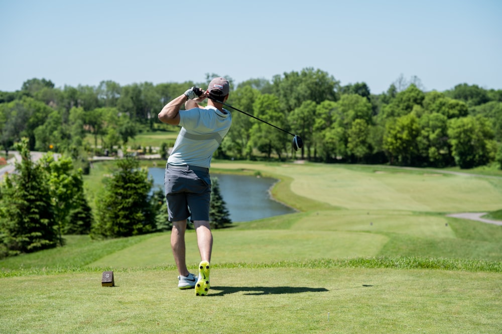 Hombre con camiseta blanca y pantalones cortos negros jugando al golf durante el día