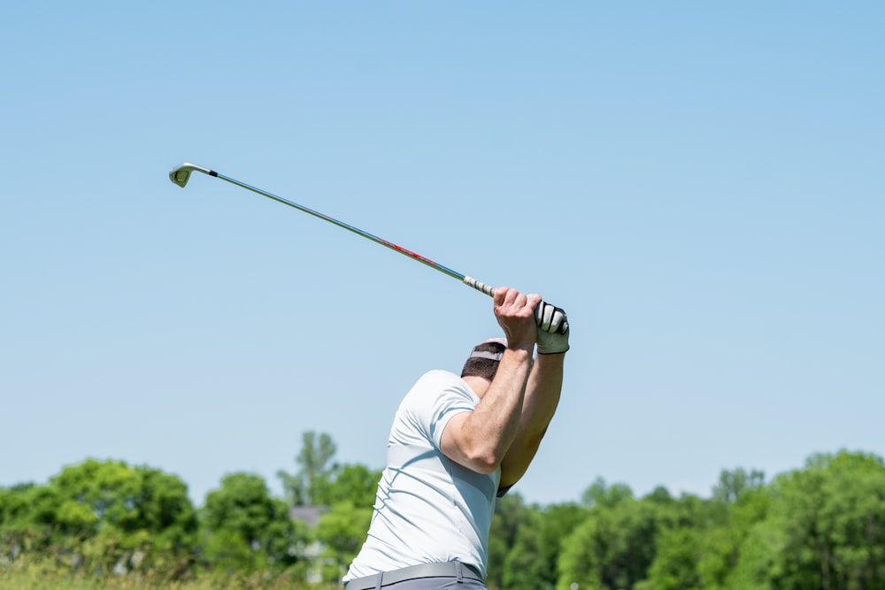 uomo in canotta bianca e pantaloncini bianchi che gioca a golf durante il giorno