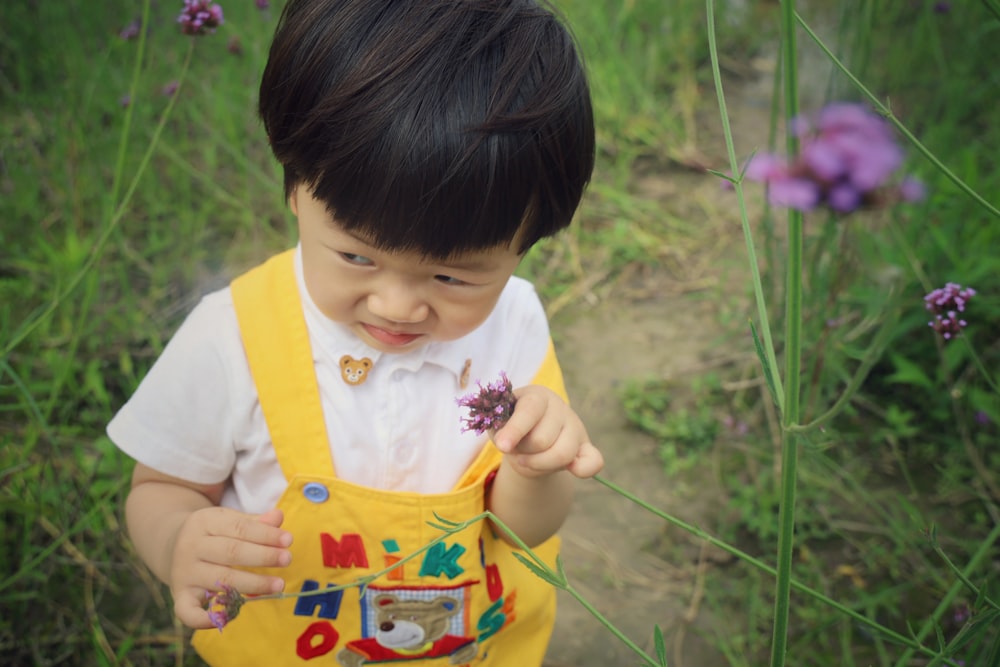 girl in yellow and white shirt holding pink flower