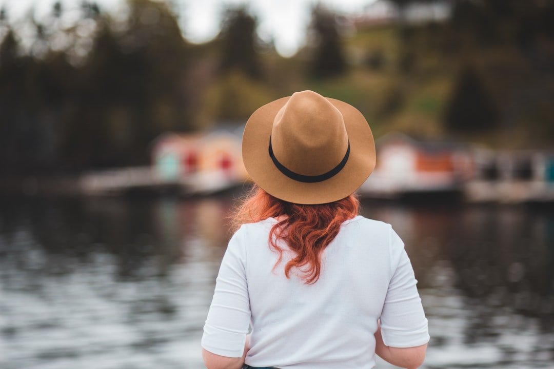 woman in white long sleeve shirt wearing brown fedora hat standing near body of water during