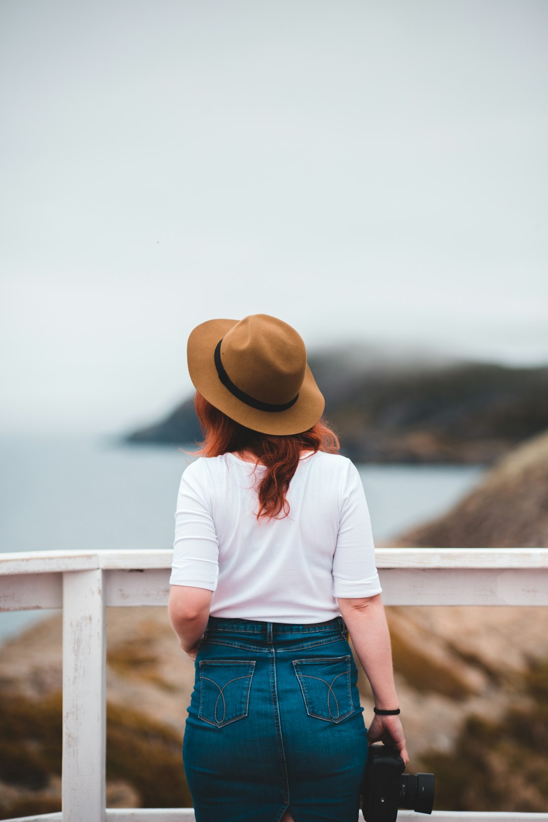 woman in white shirt and blue denim jeans wearing brown hat standing near body of water