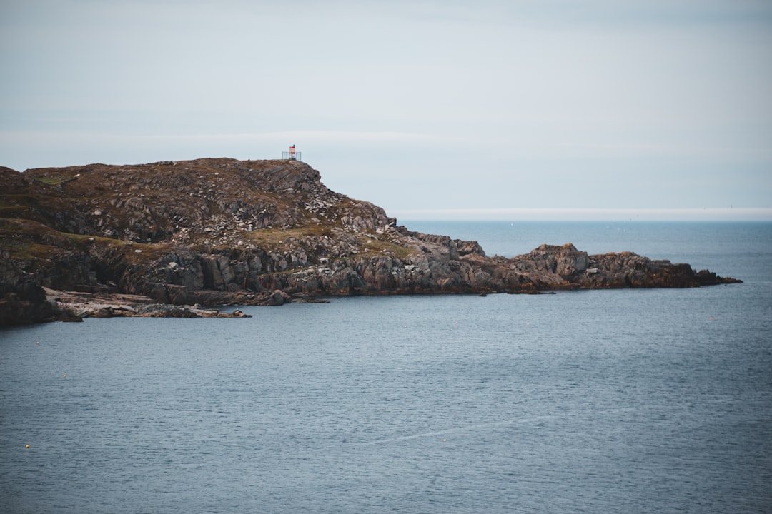 white and red lighthouse on brown rock formation in the middle of sea during daytime