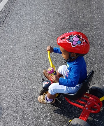 A young child with a big smile riding a bright red adaptive tricycle on a sunny day in Oxford.