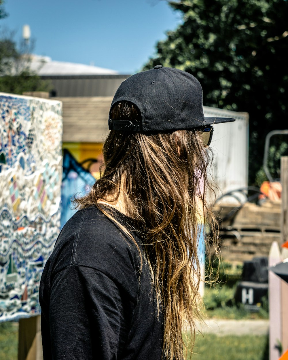 Mujer con camisa negra y gorra negra de pie cerca de la pared de graffiti durante el día