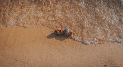 Close-up of aqua shoes on a sandy beach with gentle waves in the background.