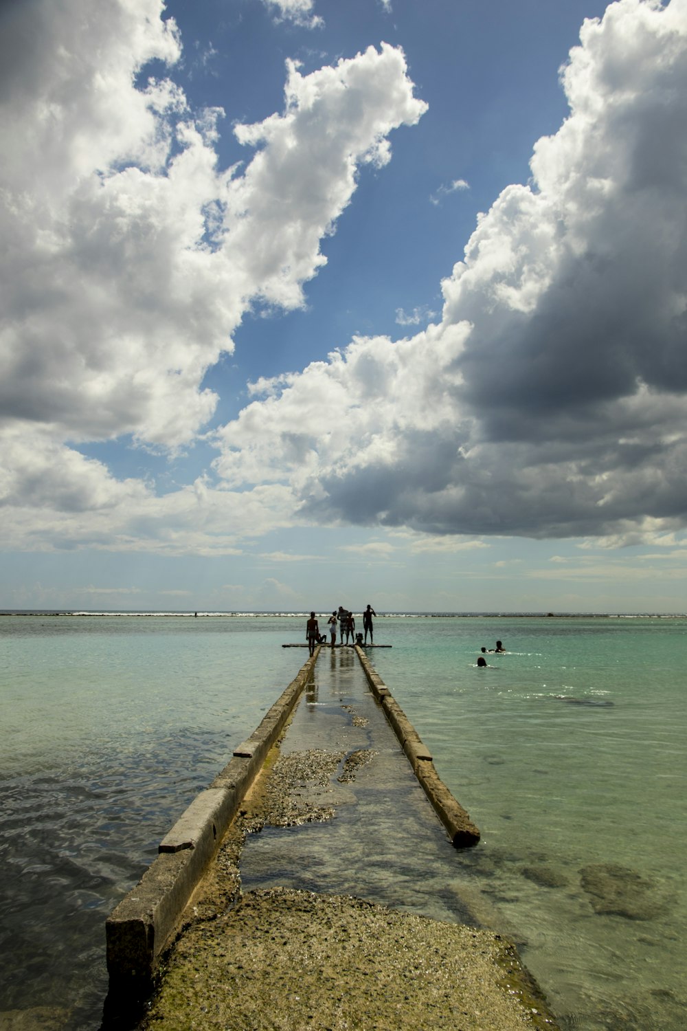 Persone che camminano sul molo di legno sotto il cielo nuvoloso blu e bianco durante il giorno