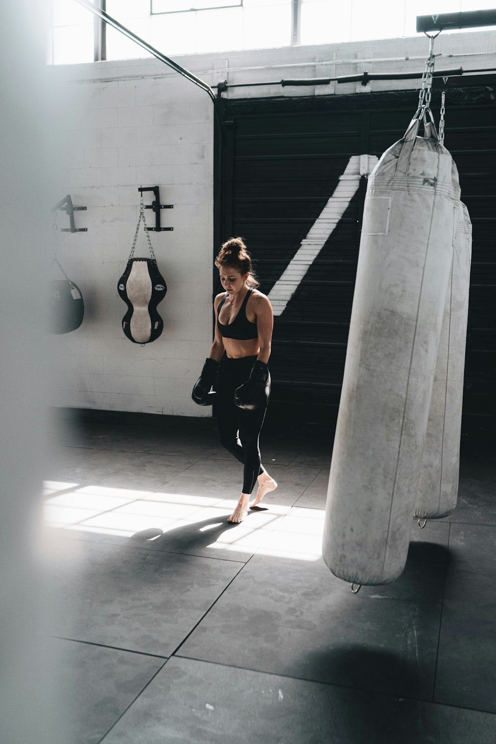 woman in black tank top and black leggings standing beside white and black heavy bag