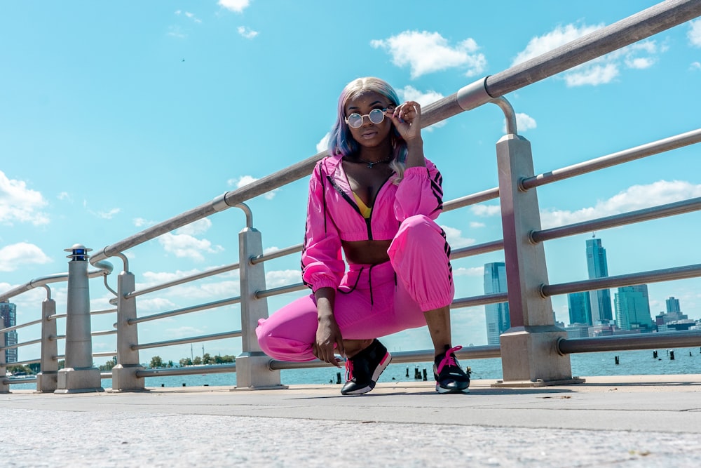 woman in pink jacket and pants sitting on brown wooden fence during daytime