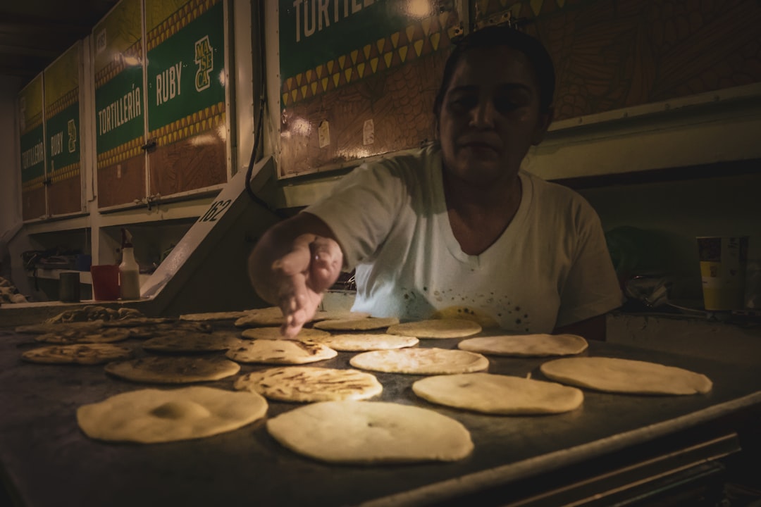 man in white crew neck t-shirt standing beside man in white crew neck t-shirt, Woman making tortillas