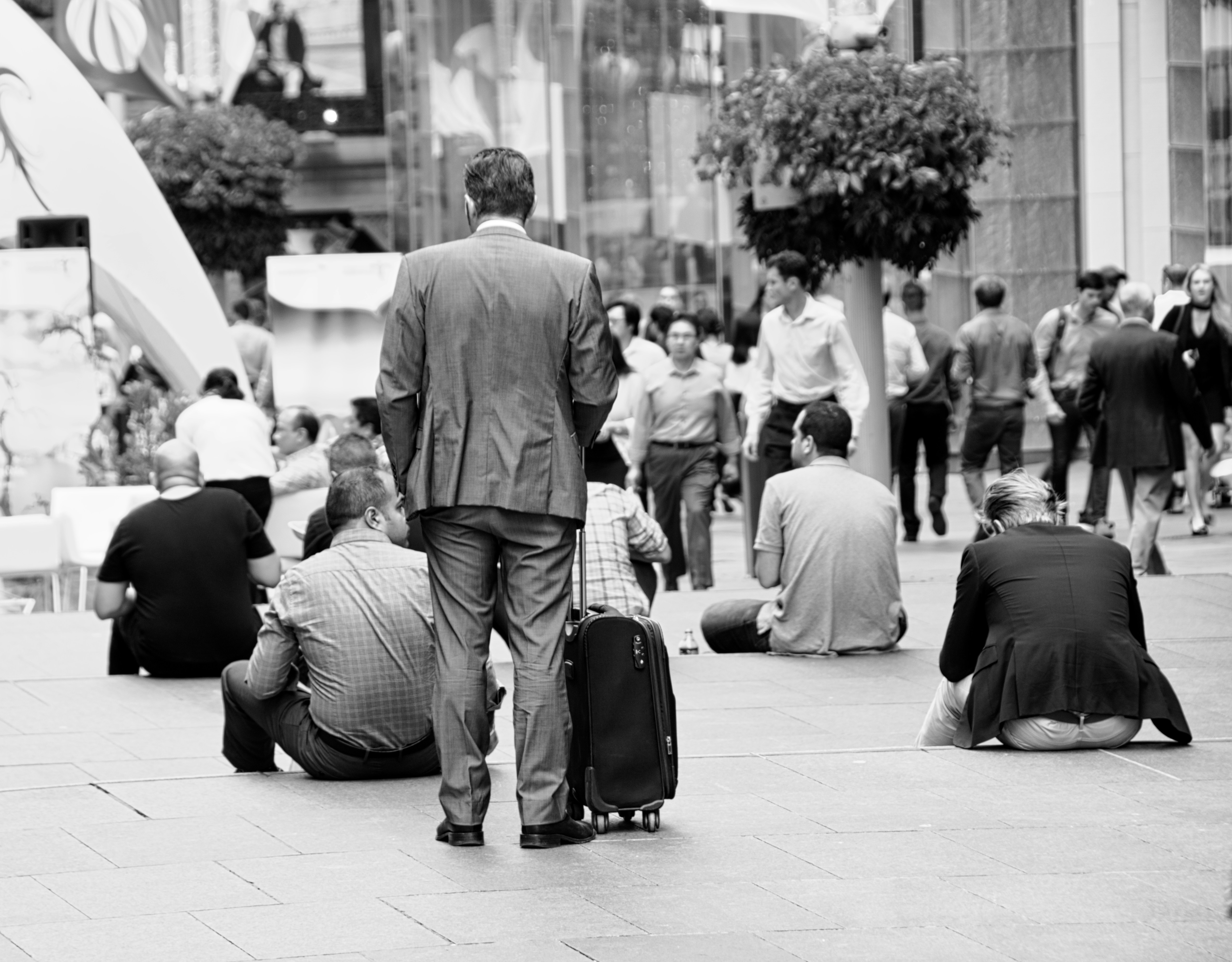 A man with a suitcase standing in the middle of people sitting down.