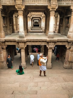 An intricately carved stepwell with multiple levels and supporting pillars. People are walking and taking photos inside the historical structure. The atmosphere seems serene and the architecture is detailed, showcasing traditional craftsmanship.