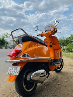 orange and black motor scooter parked on gray concrete pavement during daytime
