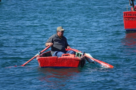 man in black shirt and brown hat riding red boat on body of water during daytime in Sagres Portugal