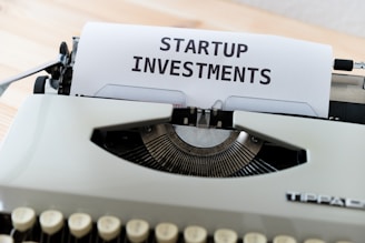 A vintage typewriter with a piece of paper displaying the text 'STARTUP INVESTMENTS'. The typewriter is a classic model with keys in focus and the paper neatly inserted into the ribbon area.